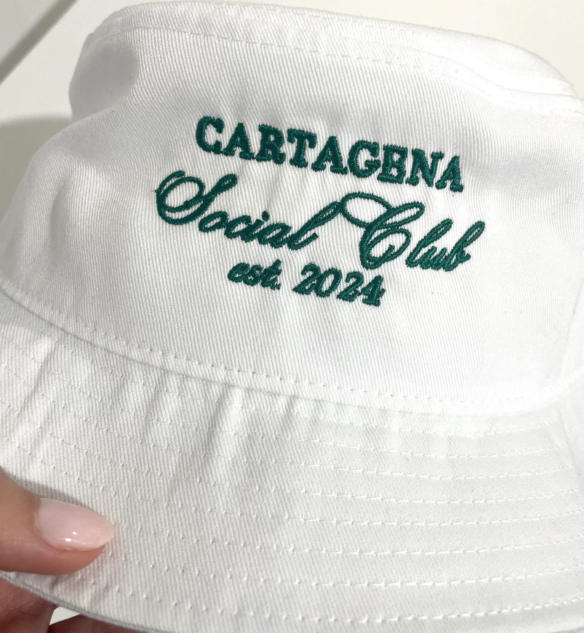 Close-up of a white bucket hat with dark green Cartagena Social Club est. 2024 embroidery.