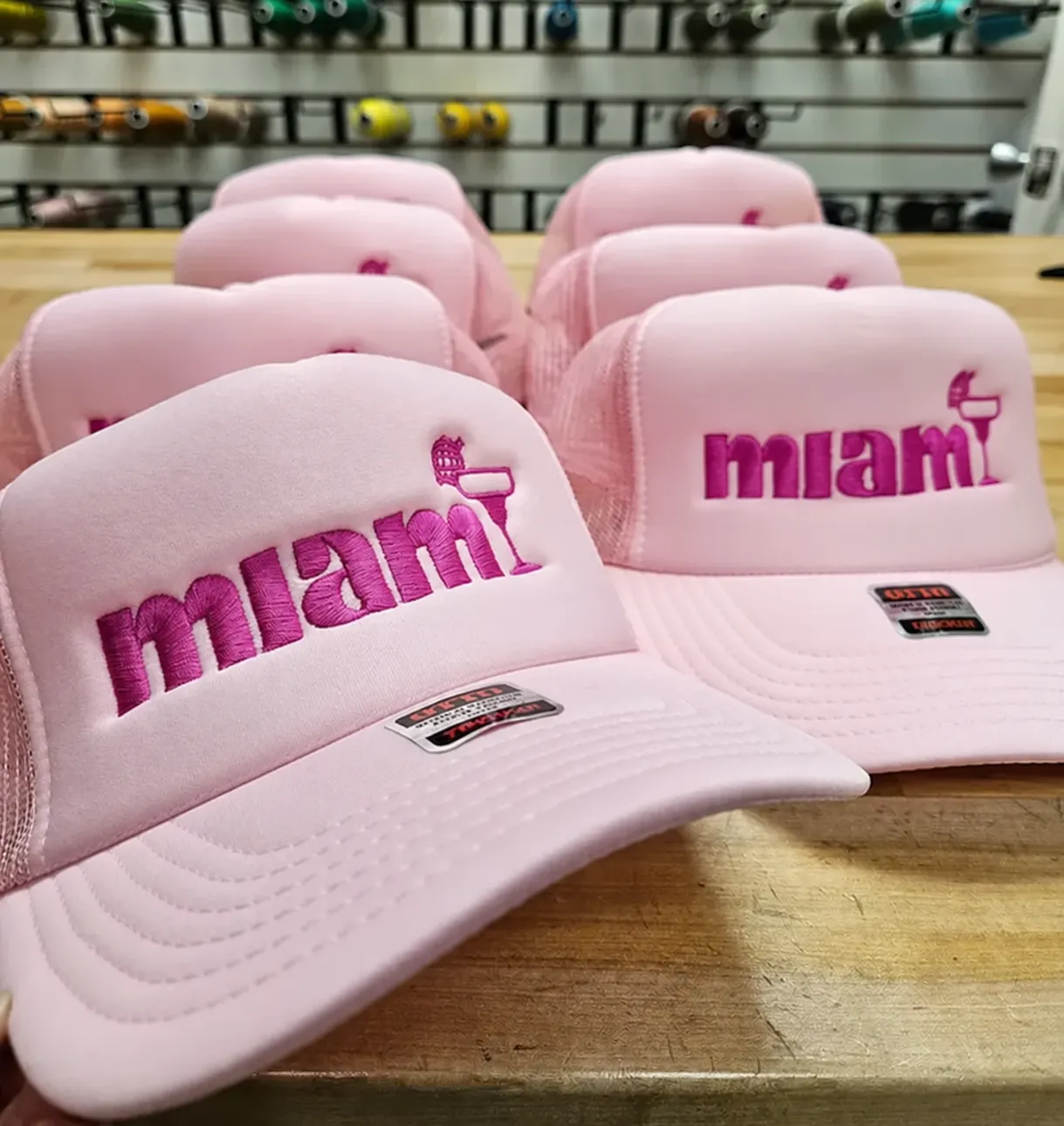 Group of pink foam trucker hats embroidered with a magenta Miami flamingo logo