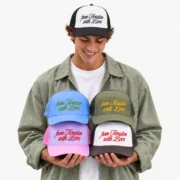 Male model wearing a black and white embroidered foam trucker hat while holding four colorful custom hats