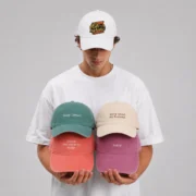 Model wearing a white embroidered 5 panel cap and holding four personalized baseball hats