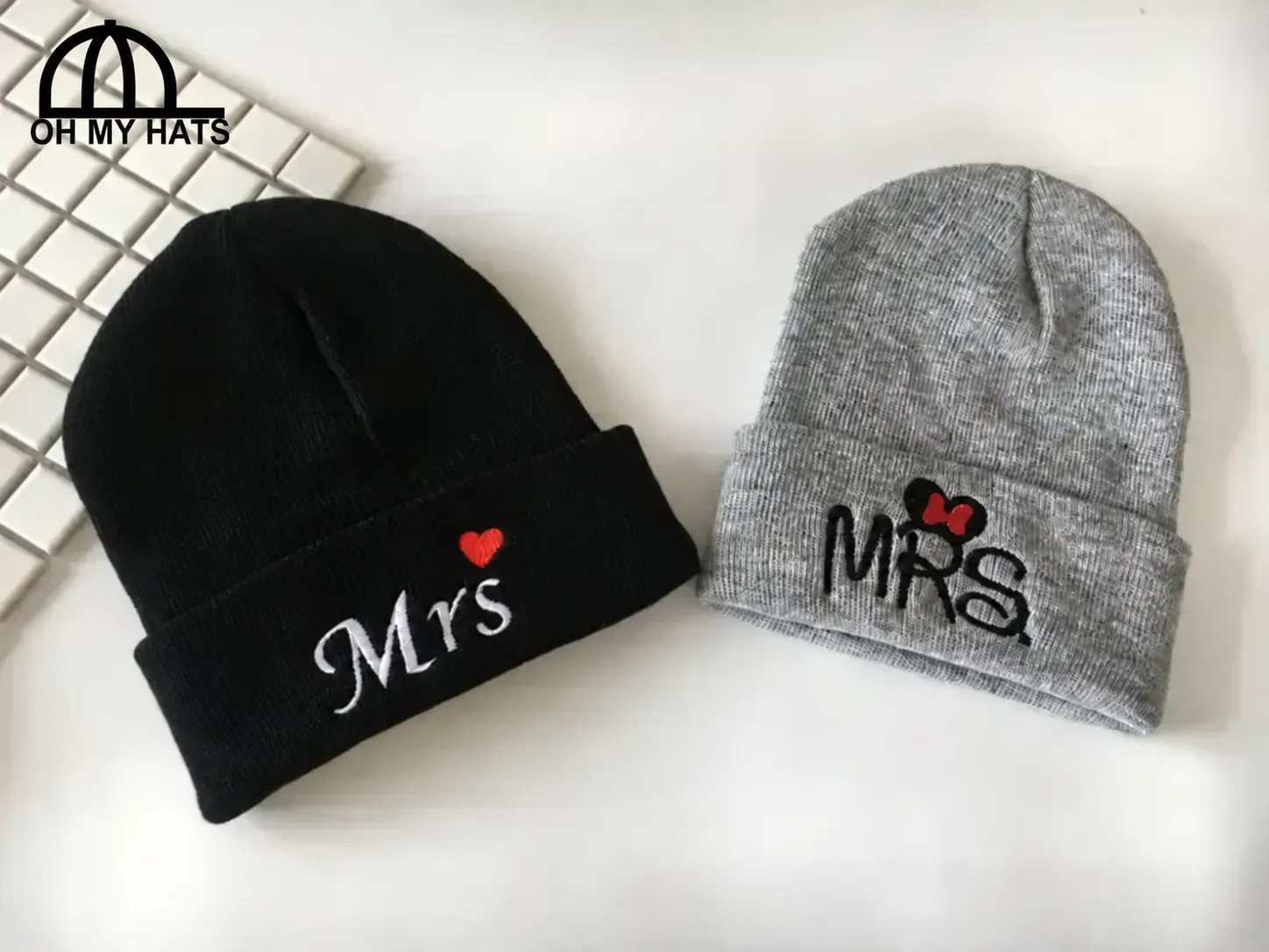 Black and gray cuffed beanies with Mrs lettering and red embroidered accents beside a white keyboard.