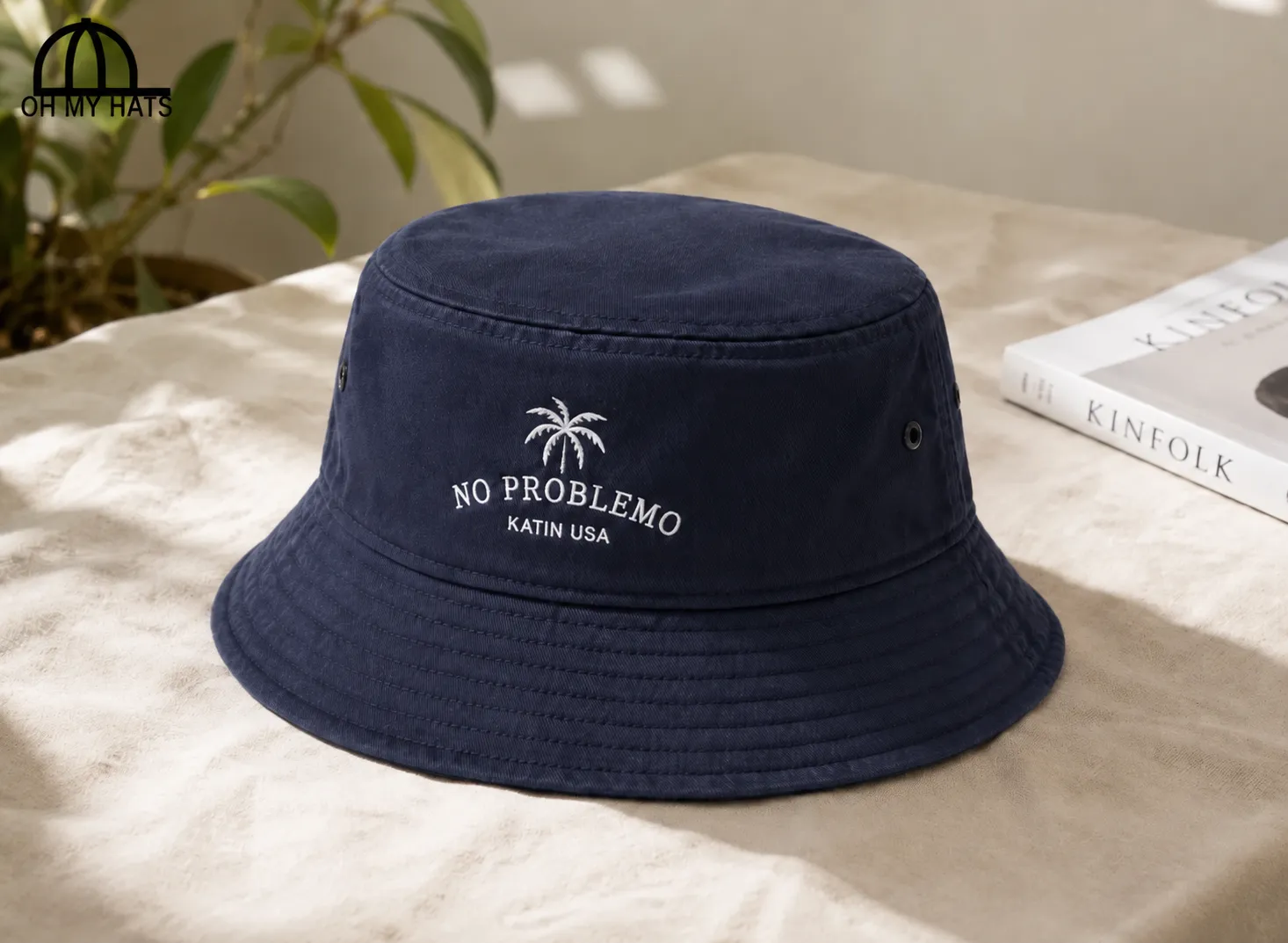 Navy bucket hat with white palm tree and NO PROBLEMO embroidery on a sunlit beige tabletop.
