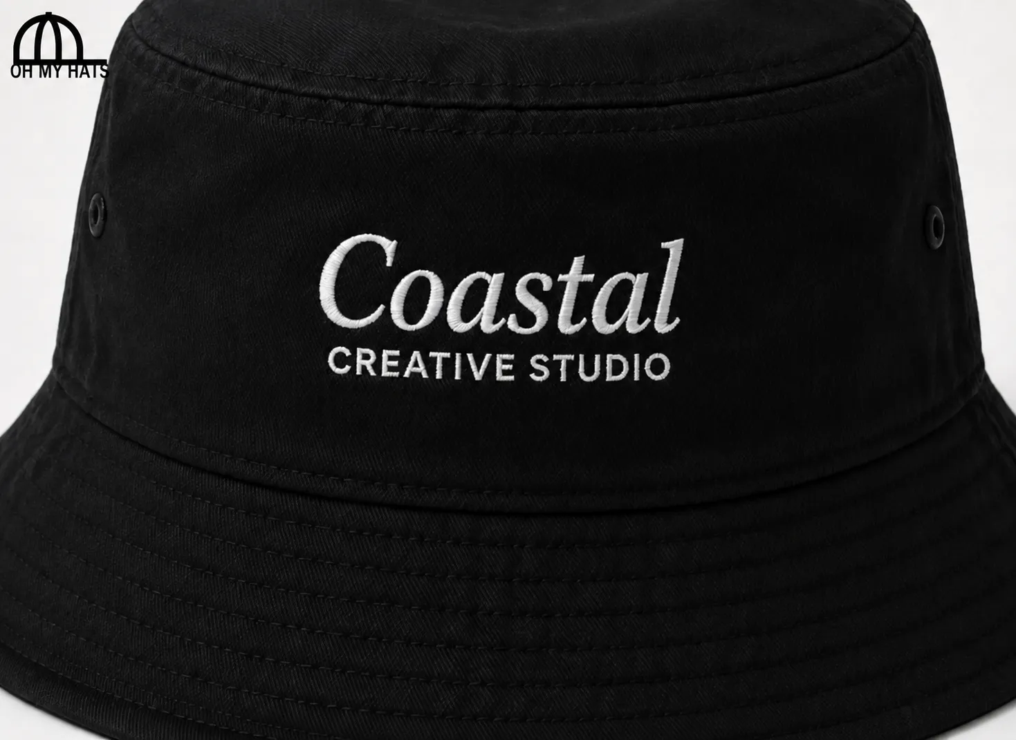 Close-up of a black bucket hat with white Coastal Creative Studio embroidery and stitched brim details.