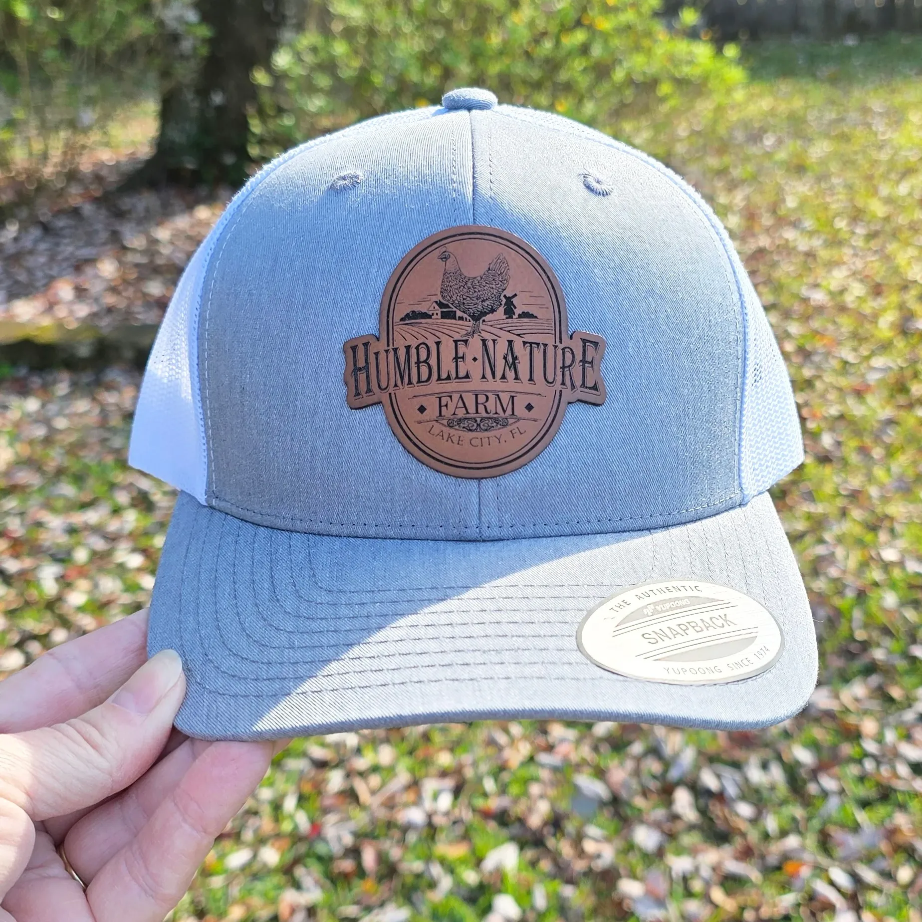 Light gray trucker hat featuring a brown Humble Nature Farm leather patch