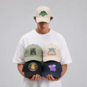 Model wearing a beige ohmyhats baseball cap and holding four custom printed baseball hats.