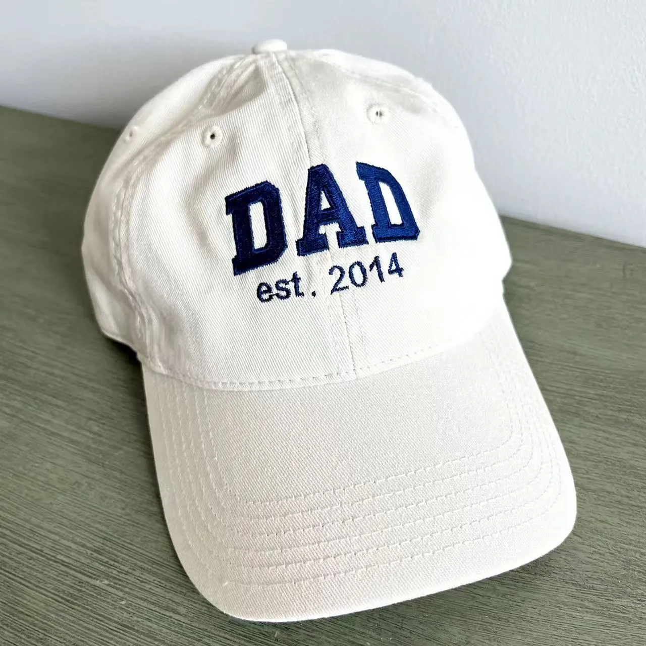 White dad hat with navy DAD est. 2014 embroidery and a curved brim.