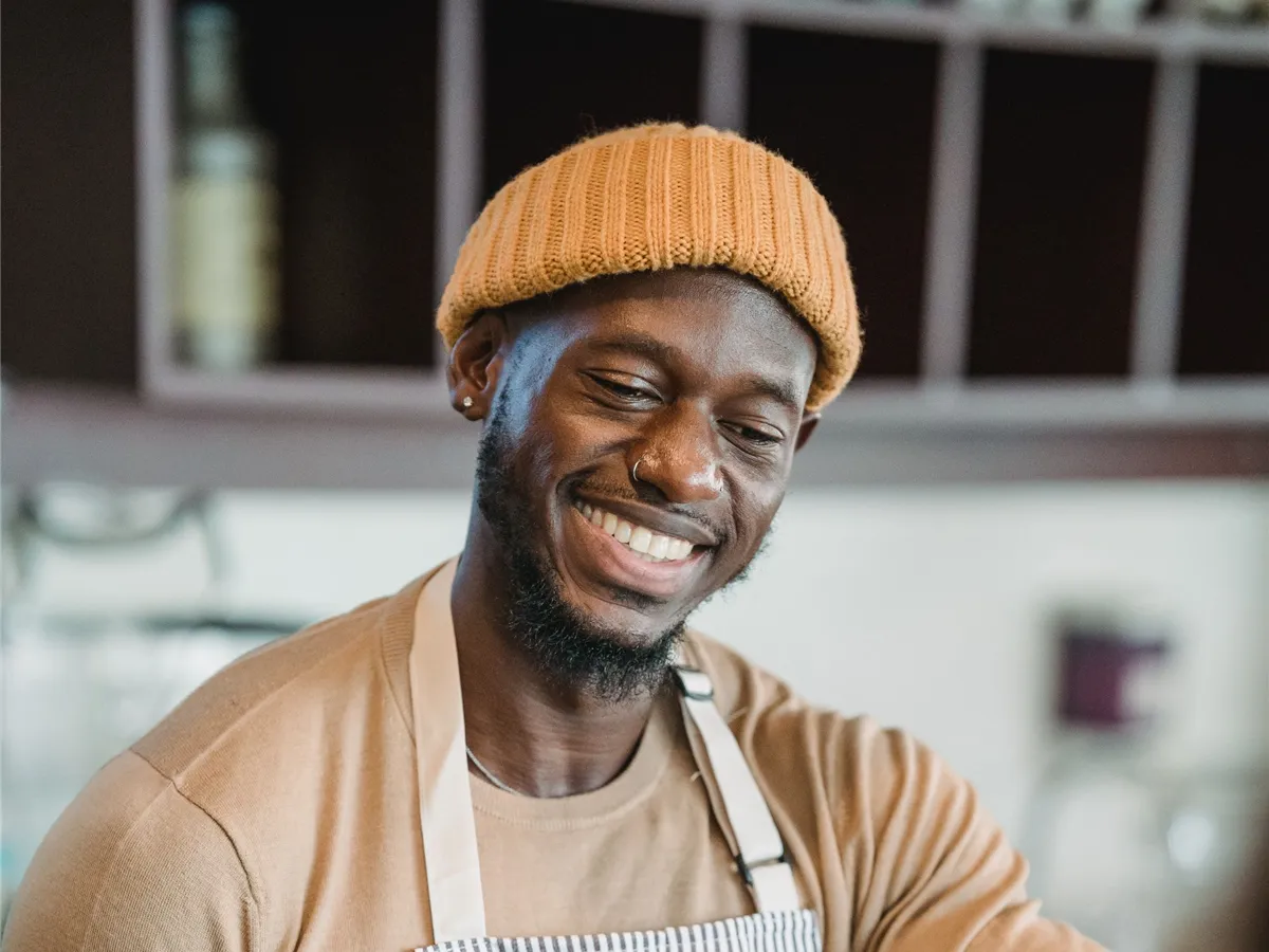 Café worker wearing a mustard knit beanie and striped apron in a café.