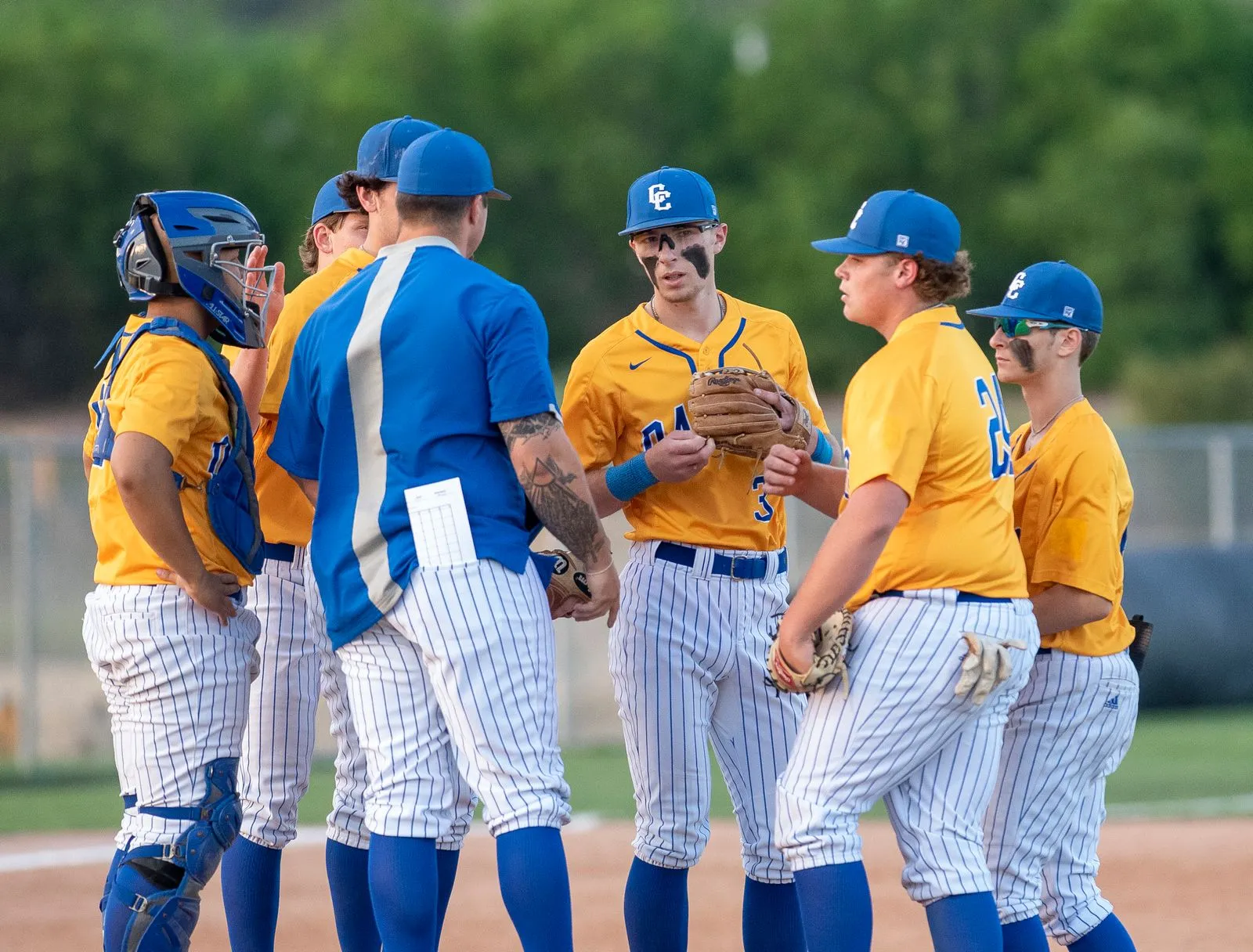 Baseball players in matching blue caps and yellow uniforms gathered with their coach on a field in Texas.