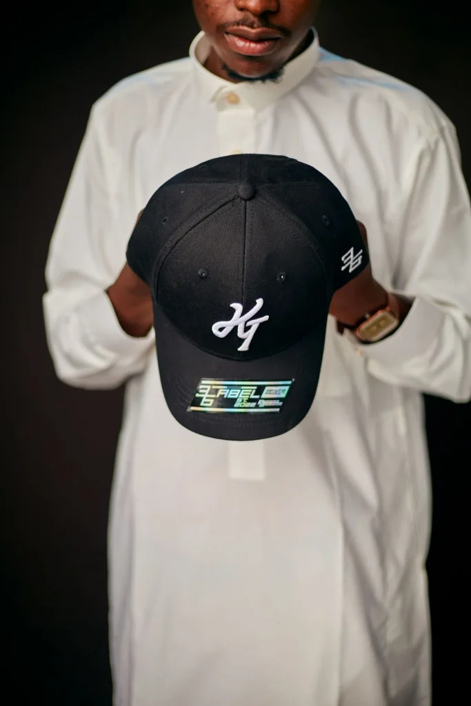 Man holding a black baseball cap with white embroidered lettering.