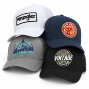 Four embroidered trucker hats in white, navy, gray, and black, arranged in an overlapping group on a white background.