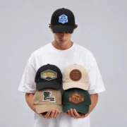 Model wearing a black OH MY HATS! patch baseball hat and holding four custom patch hats in black, beige, khaki, and dark green.