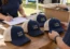 Event organizers checking navy and cream custom trucker hats beside an order checklist.