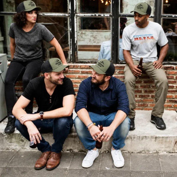 Four friends wearing olive green and black mesh trucker hats embroidered with WEEKEND CREW, seated outside a brick building.
