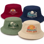 Four custom printed bucket hats in burgundy, navy, sage green, and beige, featuring floral, coastal, mountain, and sunset designs on a white background.